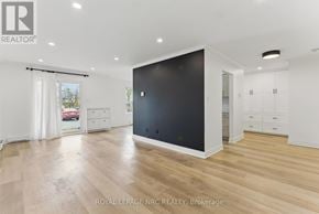 Lincoln (Beamsville) condo for rent - A spacious room with wooden flooring and white walls, featuring a large black door and a window with white curtains.
