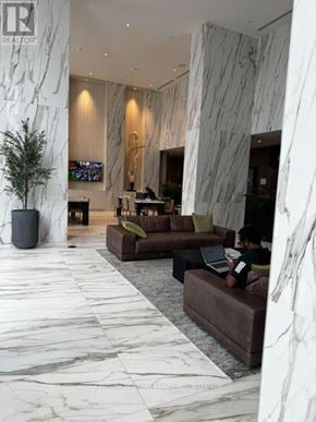 Mississauga (City Centre) condo for rent - A man is sitting on a couch in a spacious lobby with marble floors and walls.