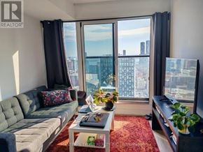 Toronto (Moss Park) condo for rent - A living room with a grey sofa, a coffee table, and a large window with a view of the city.