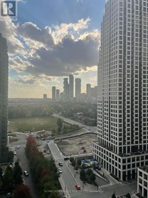 Mississauga (City Centre) condo for rent - A cityscape with a large building in the foreground and a highway in the background.