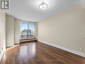 Toronto (York University Heights) condo for rent - A room with wooden floors and a large window overlooking a cityscape.