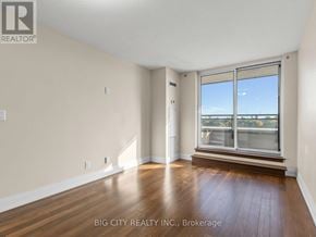 Toronto (York University Heights) condo for rent - A room with wooden floors and a large window overlooking a cityscape.