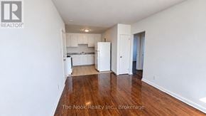 Oshawa (Lakeview) apartment for rent - A white room with wood flooring and a kitchen area in the background.
