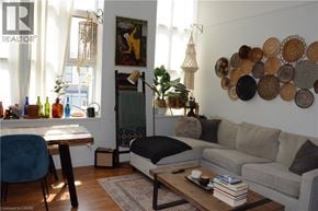 Kitchener condo for rent - A living room with a grey couch, a wooden table, a blue chair, a coffee table with a book and a remote control on it, a wall with circular decorations, and a window with curtains.