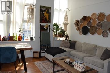 Kitchener condo for rent - A living room with a grey couch, a wooden table, a blue chair, a coffee table with a book and a remote control on it, a wall with circular decorations, and a window with curtains.