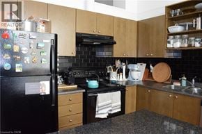 Kitchener condo for rent - A black refrigerator with magnets on it is in a kitchen with wooden cabinets.