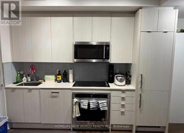 Toronto (Annex) condo for rent - A kitchen with white cabinets and a black microwave above the stove.