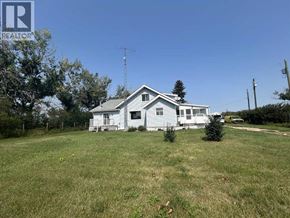 Rural Kneehill County apartment for rent - A white house with a grey roof is surrounded by a grassy field.