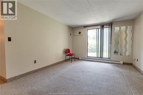 Windsor condo for rent - A room with a carpeted floor, a window with a view of trees, and a red chair.