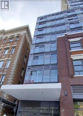 Toronto (Kensington-Chinatown) condo for rent - A building with the number 231 on it is in front of a taller building.