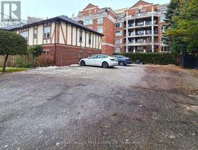 Toronto (Kingsway South) multi-family for rent - A car is parked in a gravel lot in front of a building.