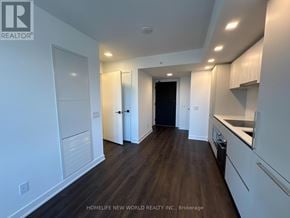 Toronto (North St. James Town) condo for rent - A spacious kitchen with white cabinets and a black door at the end of the hallway.