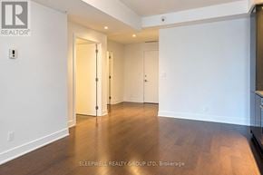 Ottawa condo for rent - A room with white walls and wooden flooring, with a door on the left and a kitchen area on the right.
