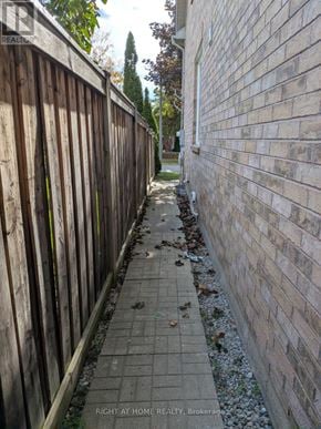 Mississauga (Churchill Meadows) apartment for rent - A narrow sidewalk runs between a wooden fence and a brick wall.