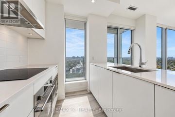 Toronto (Newtonbrook East) condo for rent - A modern kitchen with white cabinets and a large window overlooking the city.