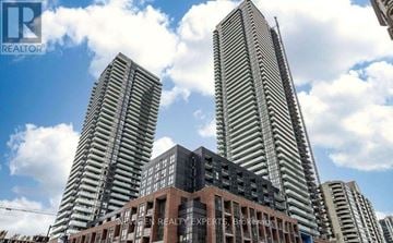 Mississauga (City Centre) condo for rent - Two tall buildings stand behind a smaller building with a sign that says "REALTOR".