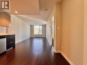 Vancouver apartment for rent - A spacious room with wooden floors and a kitchen area with black cabinets.