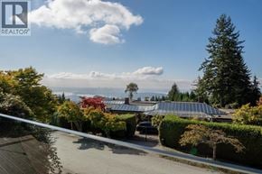 West Vancouver apartment for rent - A house with a roof covered in solar panels is surrounded by trees and bushes.