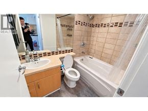 Vancouver apartment for rent - A man is taking a photo of a bathroom with a toilet, sink, and bathtub.