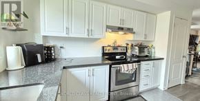 Oshawa (Windfields) townhouse for rent - A kitchen with white cabinets and a black countertop.