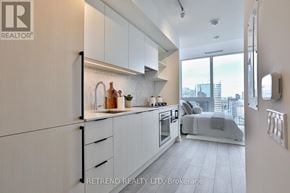 Toronto (Church-Yonge Corridor) condo for rent - A modern kitchen with white cabinets and appliances, a large window with a view of the city, and a bed in the background.