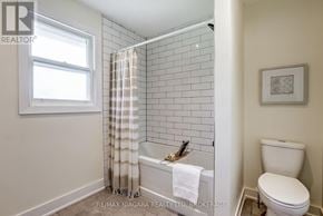 Niagara Falls (Dorchester) apartment for rent - A white toilet sits next to a white bathtub in a bathroom with white walls.