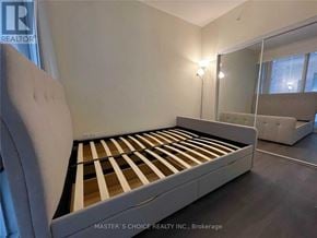 Toronto (Bay Street Corridor) condo for rent - A bed with a white headboard and wooden slats is in a room with a mirror and a lamp.