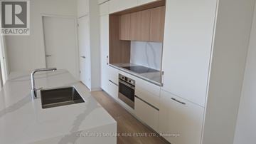 Toronto (Annex) condo for rent - A modern kitchen with white cabinets and a wooden hood.