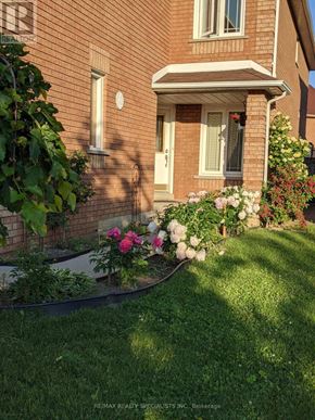 Mississauga (Lisgar) apartment for rent - A house with a white door and windows is surrounded by a garden with flowers.