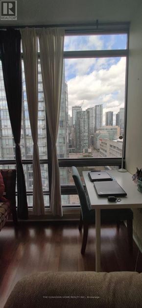 Toronto (Waterfront Communities) condo for rent - A room with a desk and chair in front of a window with a view of a city skyline.