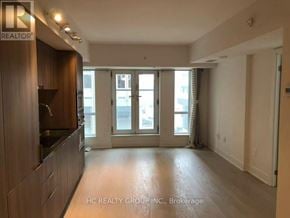 Toronto (Bay Street Corridor) condo for rent - A spacious living room with a kitchen area to the left and a sliding glass door leading to a balcony.