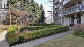 Brampton (Fletcher's Creek South) condo for rent - A residential area with a building, a tree, and a hedge.