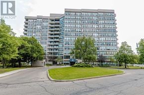 Brampton (Queen Street Corridor) condo for rent - A large building with many windows is surrounded by trees and grass.