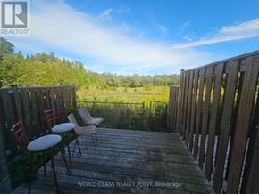 Oshawa (Samac) townhouse for rent - A wooden deck with two chairs and a table overlooking a green landscape.
