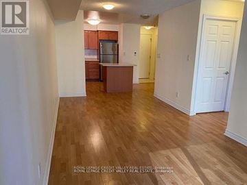 Mississauga (City Centre) condo for rent - A room with wooden floors and white walls, with a kitchen area in the background.