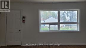 Wasaga Beach multi-family for rent - A room with a window showing a view of a house and trees.