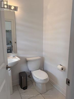 Wasaga Beach townhouse for rent - A white toilet in a small bathroom with a trash can and a sink.