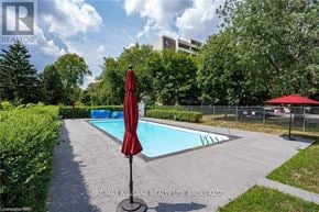 St. Catharines (Fairview) condo for rent - A pool with a red umbrella in the foreground and a building in the background.