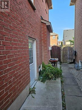 Brampton (Northwest Sandalwood Parkway) apartment for rent - A narrow alley between two red brick buildings with a white door and a wooden fence.