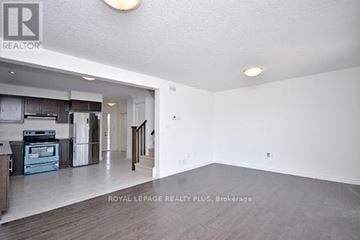 Guelph (Grange Road) townhouse for rent - A spacious living room with a kitchen in the background and a staircase leading to another floor.