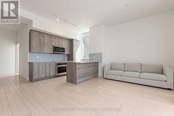 Toronto (Annex) condo for rent - A modern kitchen with a microwave above the oven and a couch in the living room.