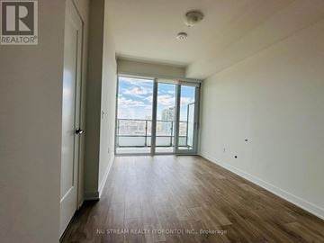Toronto (Moss Park) condo for rent - A room with wooden floors and a large window with a view of the city.