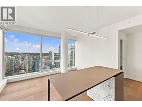 Vancouver apartment for rent - A large brown table is in the middle of a white room with a view of a city.