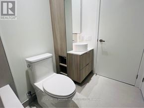 Mississauga (Port Credit) condo for rent - A white toilet in a bathroom with a wooden cabinet and mirror.