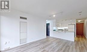 Toronto (Willowdale East) condo for rent - A spacious, empty room with white walls and a kitchen area in the background.
