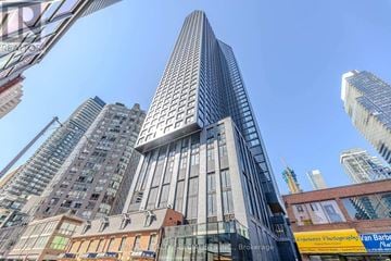 Toronto (Bay Street Corridor) condo for rent - A tall skyscraper with a glass facade stands in the middle of a cityscape.