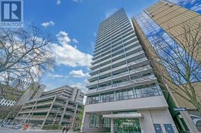 Toronto (Kensington-Chinatown) condo for rent - A tall building with a glass facade stands in front of a shorter building with a white facade.