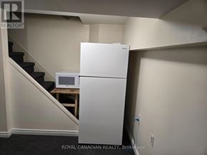 Mississauga (Cooksville) apartment for rent - A white refrigerator is in a corner of a room with a staircase.