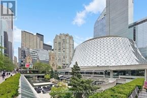 Toronto (Waterfront Communities) condo for rent - A modern building with a glass facade is surrounded by other buildings and trees.