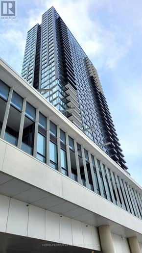 Mississauga (City Centre) condo for rent - A tall building with a glass facade stands behind a white building with a lot of windows.